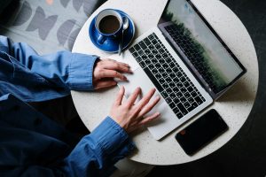 person in blue denim jeans using macbook pro beside white ceramic mug on white table